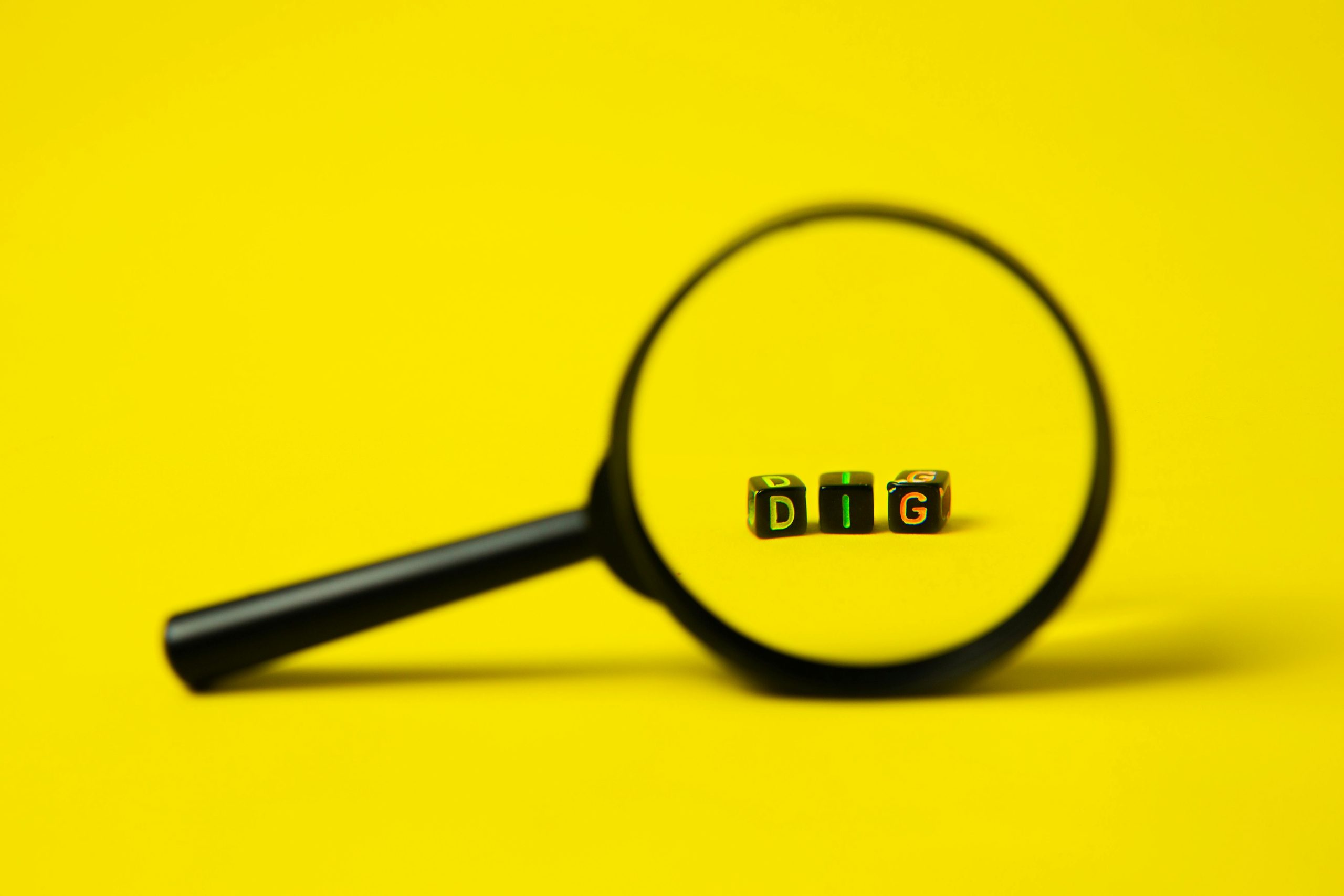 Magnifying glass focusing on letter blocks spelling "DIG" on a yellow background.